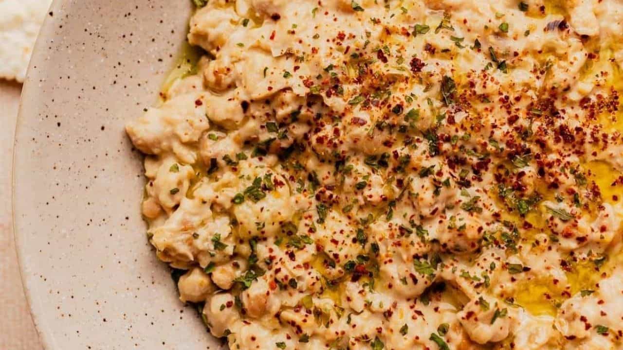 A bowl of chunky hummus garnished with olive oil, herbs, and red pepper flakes.