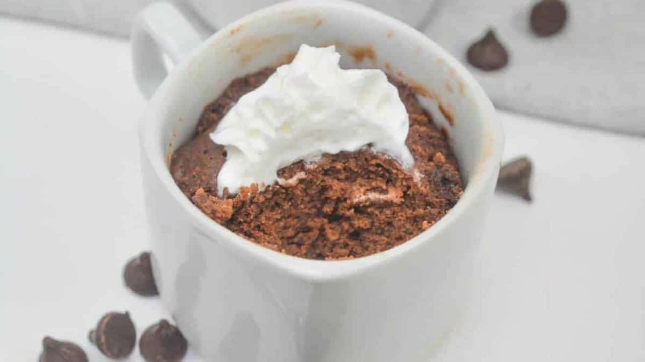 Homemade chocolate mug cake topped with whipped cream, served with a spoon and a small nutella jar on the side.