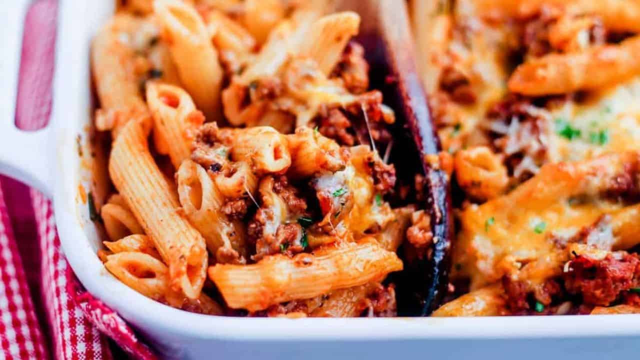 A wooden spoon scooping a portion of penne pasta bake.
