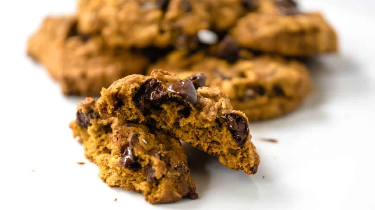 Pile of pumpkin oatmeal chocolate chip cookies with more in the background on a cooling rack.