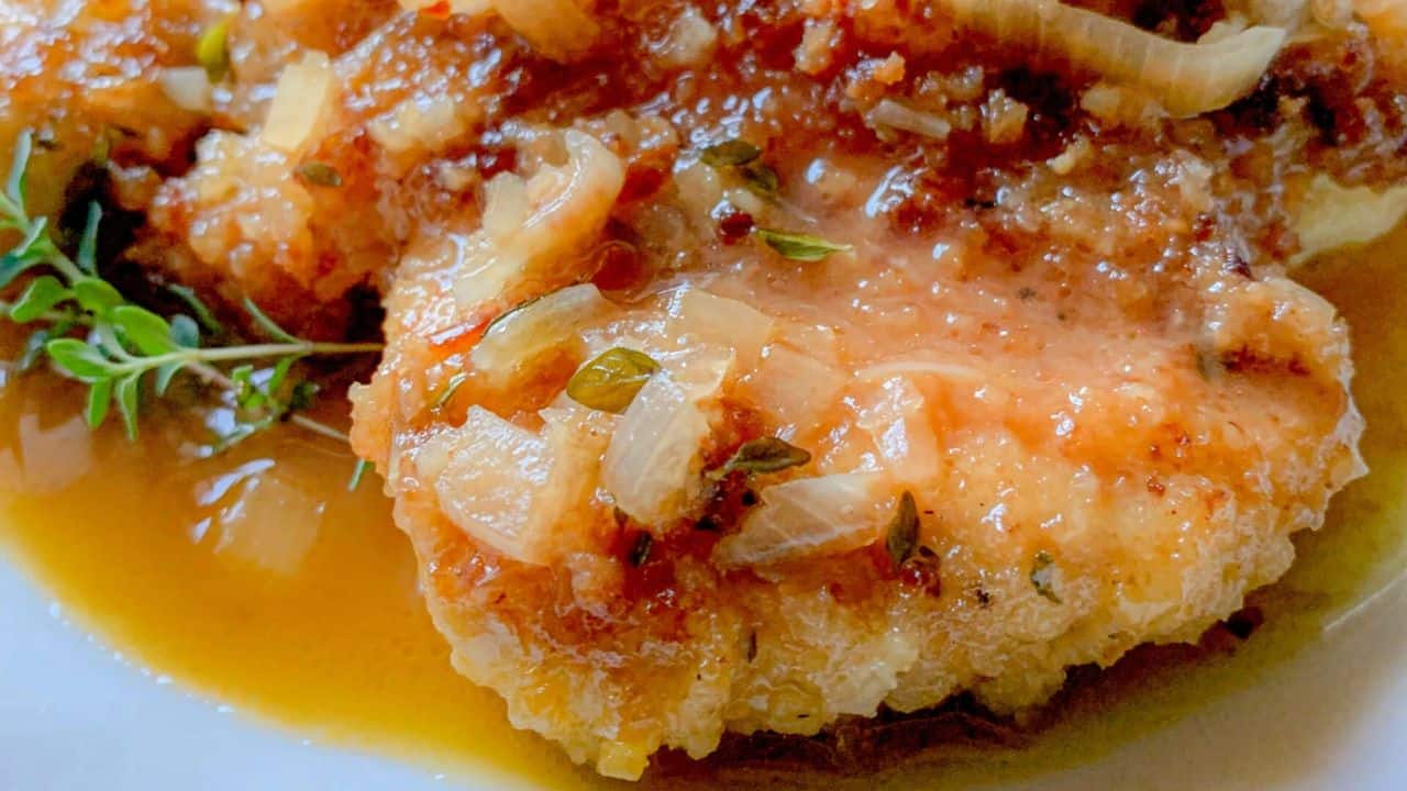 A pan-fried chicken cutlet with apple cider sauce and shallots on a plate.