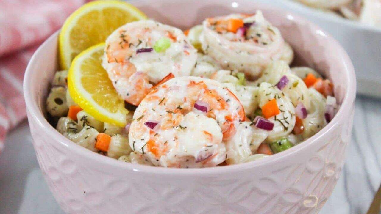 Shrimp macaroni salad in a pink bowl with lemon wedges.