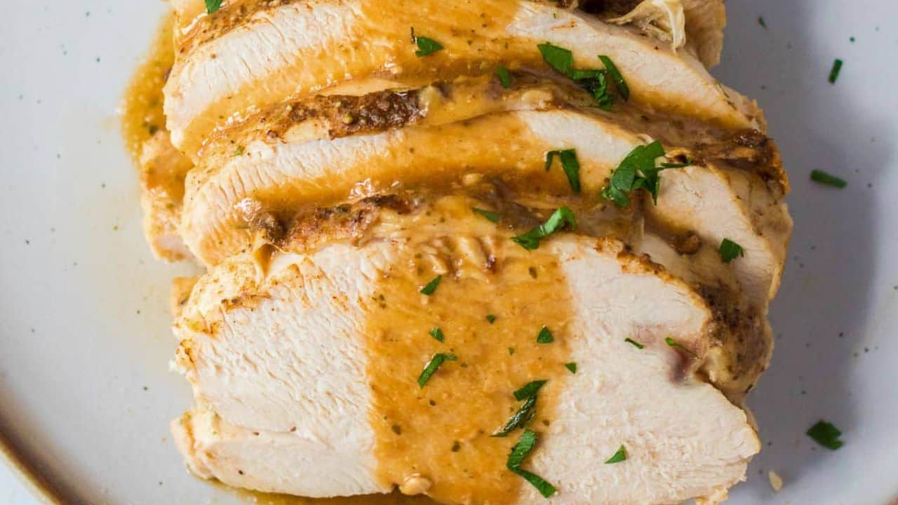 Slow Cooker Turkey Breast on a plate with gravy, stuffing, mashed potatoes and a roll.