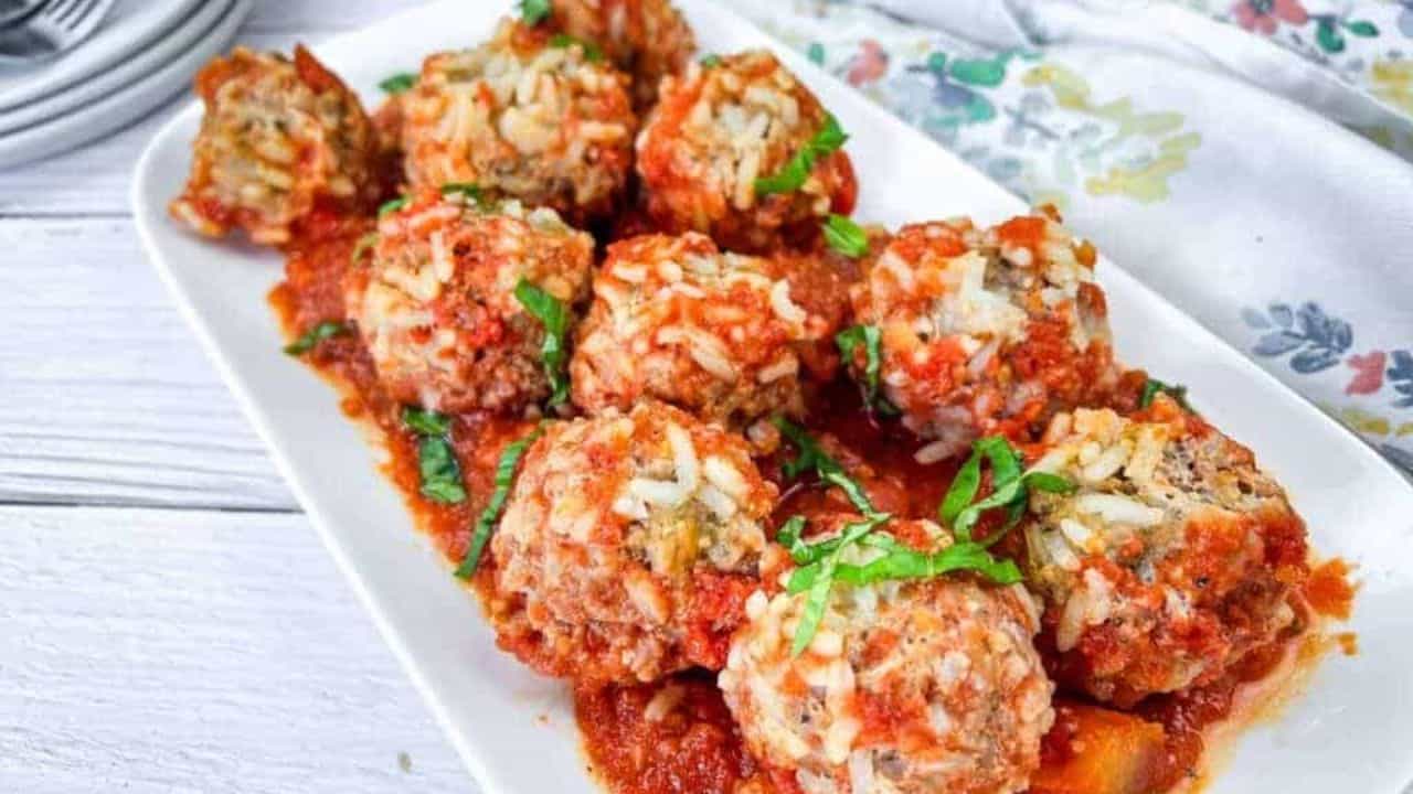 A plate of porcupine meatballs covered in tomato sauce and garnished with fresh basil.