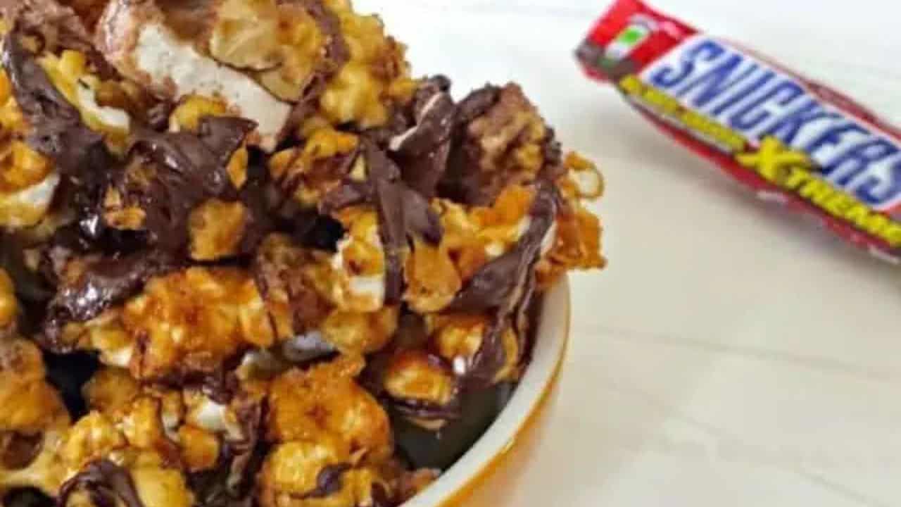 Image shows a bowl with Snickers Popcorn next to a Snicker's bar.