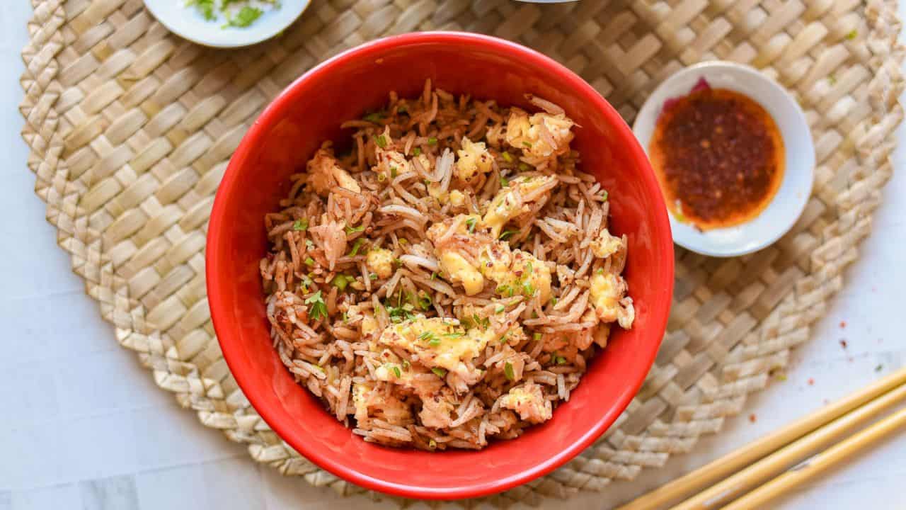 A pan of Spicy Egg Fried Rice with scrambled eggs, garnished with seasonings and stirred with a wooden spatula.