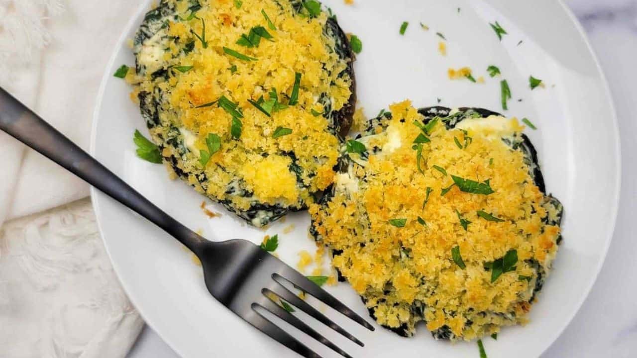 Two spinach-stuffed portobello mushrooms on a white plate.