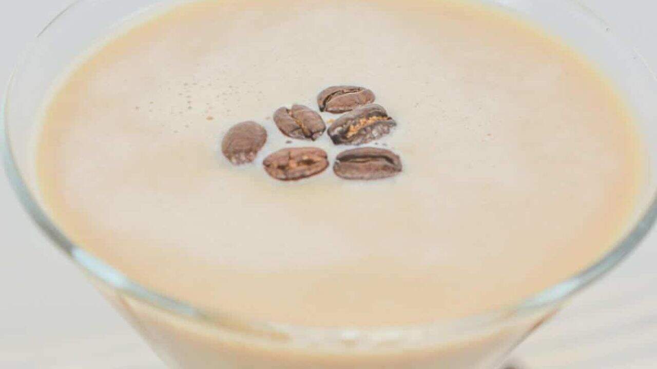 A creamy coffee drink in a martini glass, topped with coffee beans, on a striped cloth with scattered beans around.