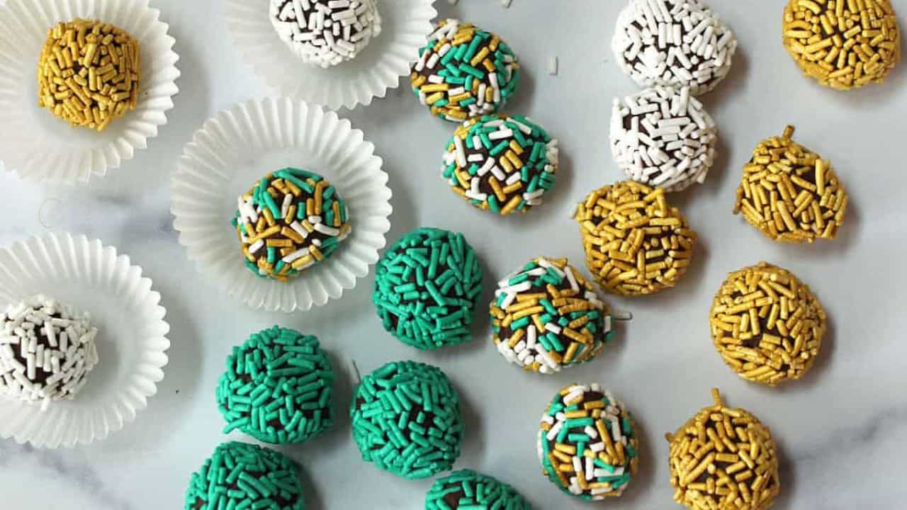 Green, gold and white sprinkle covered truffles on a white pedestal.