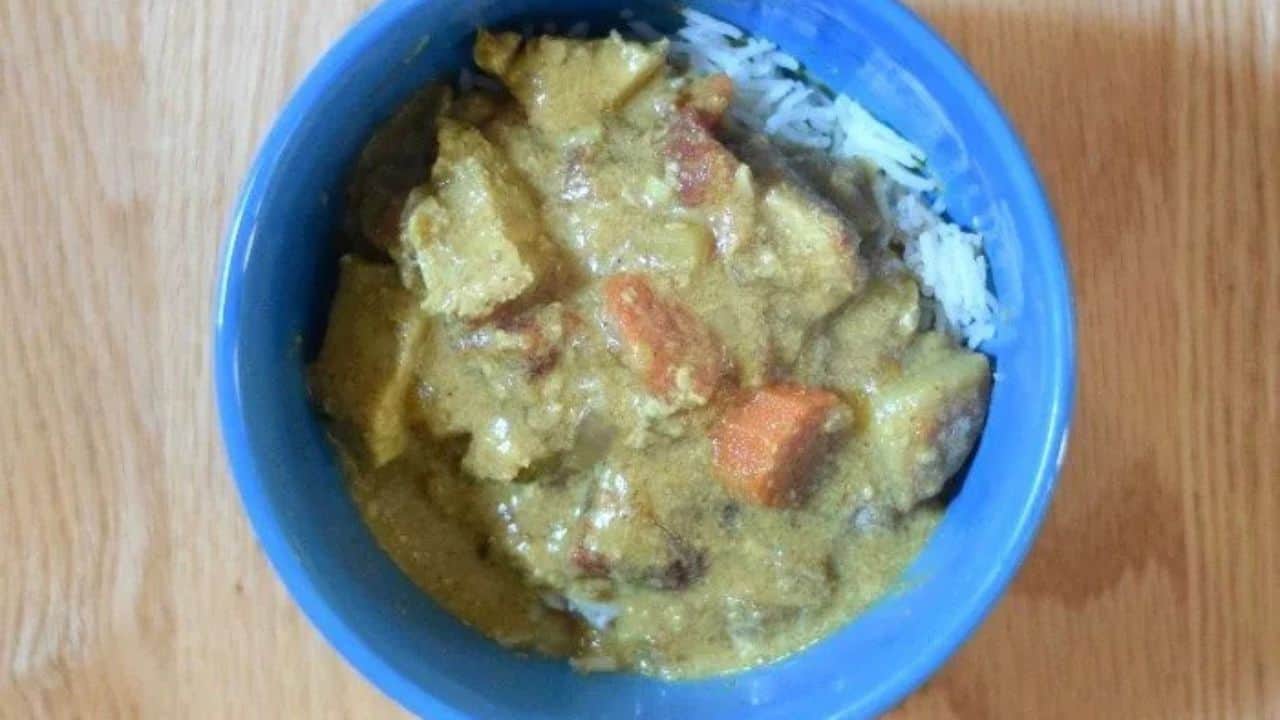 Image shows a Bite of chicken curry on a fork with the rest of the bowl in the background.