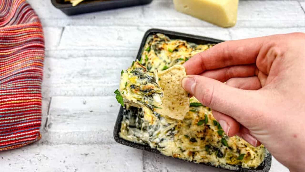 A hand dipping a tortilla chip into a tray of Copycat Applebee’s spinach artichoke dip.