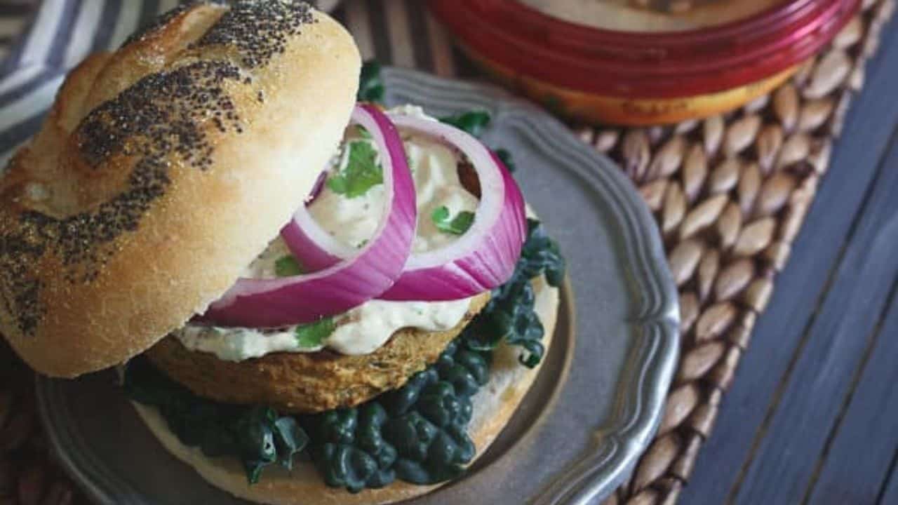 Roasted eggplant curry burger on a bun with kale, red onions and cilantro hummus sauce.