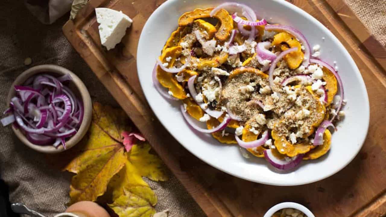 A plate of roasted squash, onions and feta on a wooden cutting board.