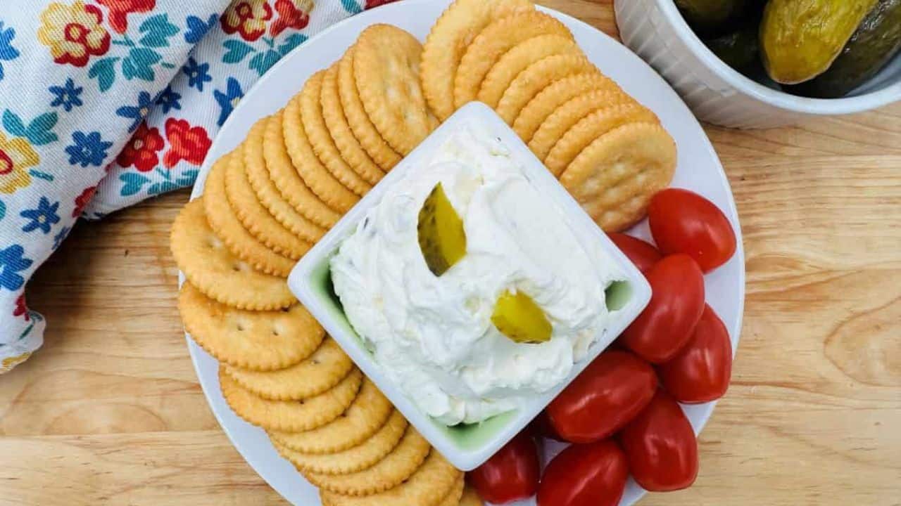 Pickle dip with crackers and tomatoes on a plate.