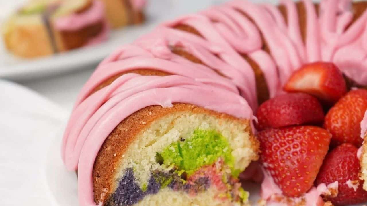 Easter bundt cake with pink icing and colorful marble swirl, sliced and served with fresh strawberries on a white plate.