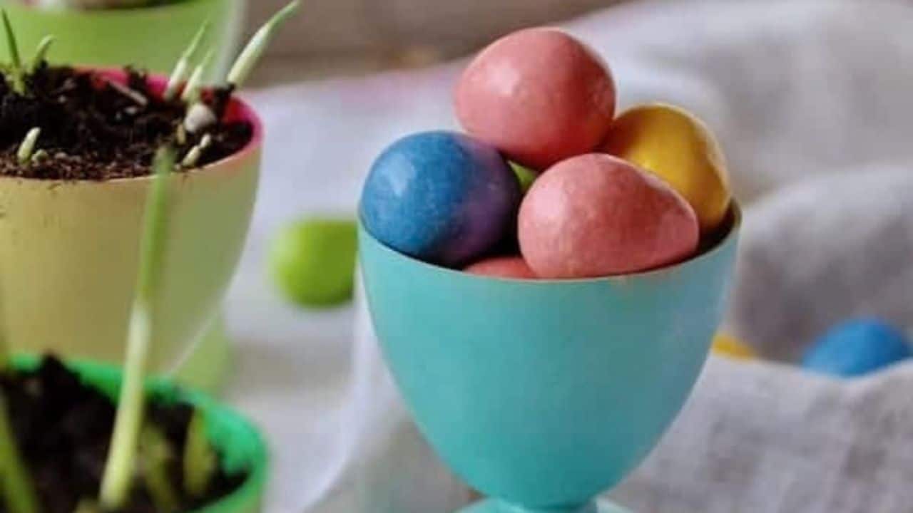 Colorful plastic Easter egg cups scattered on a wooden surface next to cans of spray paint.