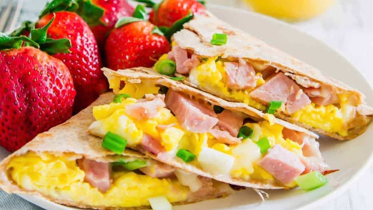 A plate of breakfast quesadillas with strawberries and ham.