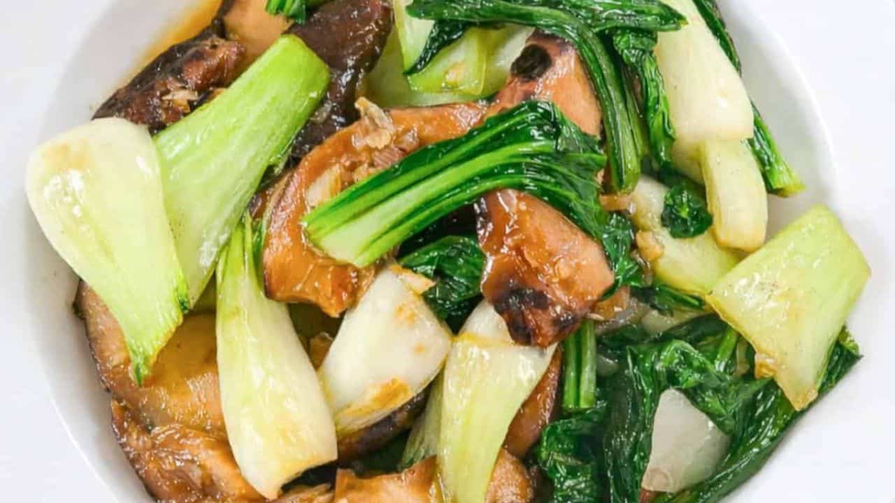 Stir fried bok choy with shiitake mushrooms served in a white bowl on a light background.