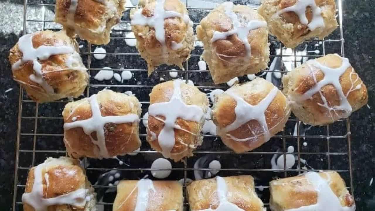 Image shows a hot cross bun with icing sitting on a plate.
