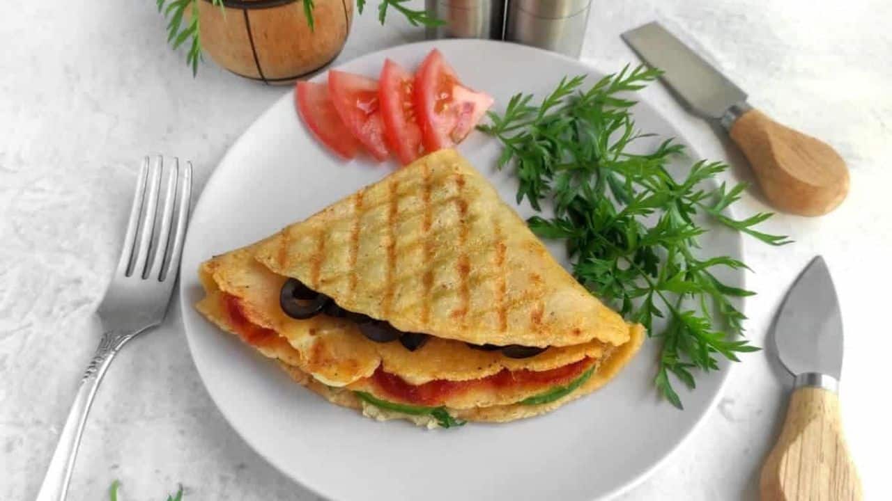 Halved lentil quesadillas on a white plate, garnished with fresh herbs, next to a fork.