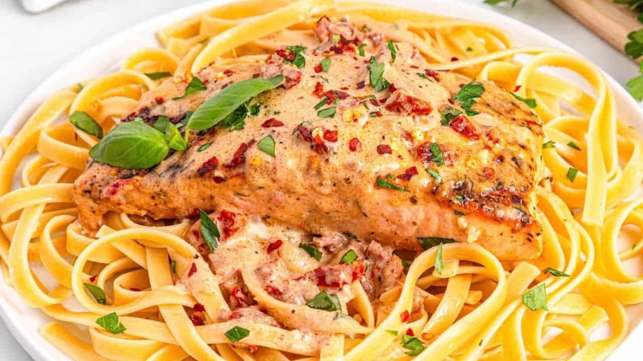 A plate of fettuccine pasta topped with creamy Marry Me Salmon, fresh basil leaves, chopped herbs, and a sprinkle of red pepper flakes.
