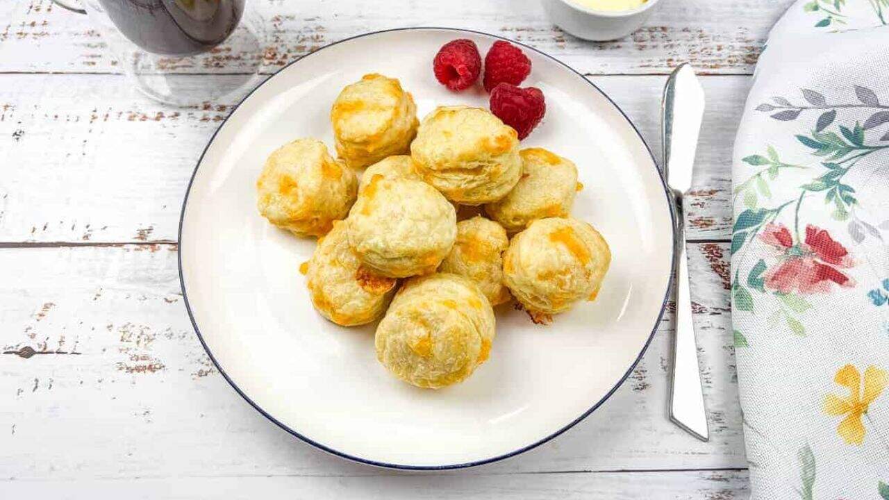 A plate of mini flaky cheese biscuits and a cup of coffee.
