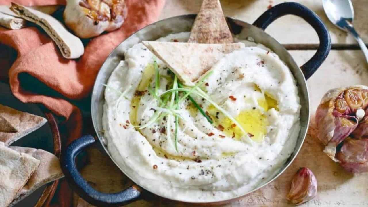 Roasted garlic white bean dip in a metal dish with pita chips.