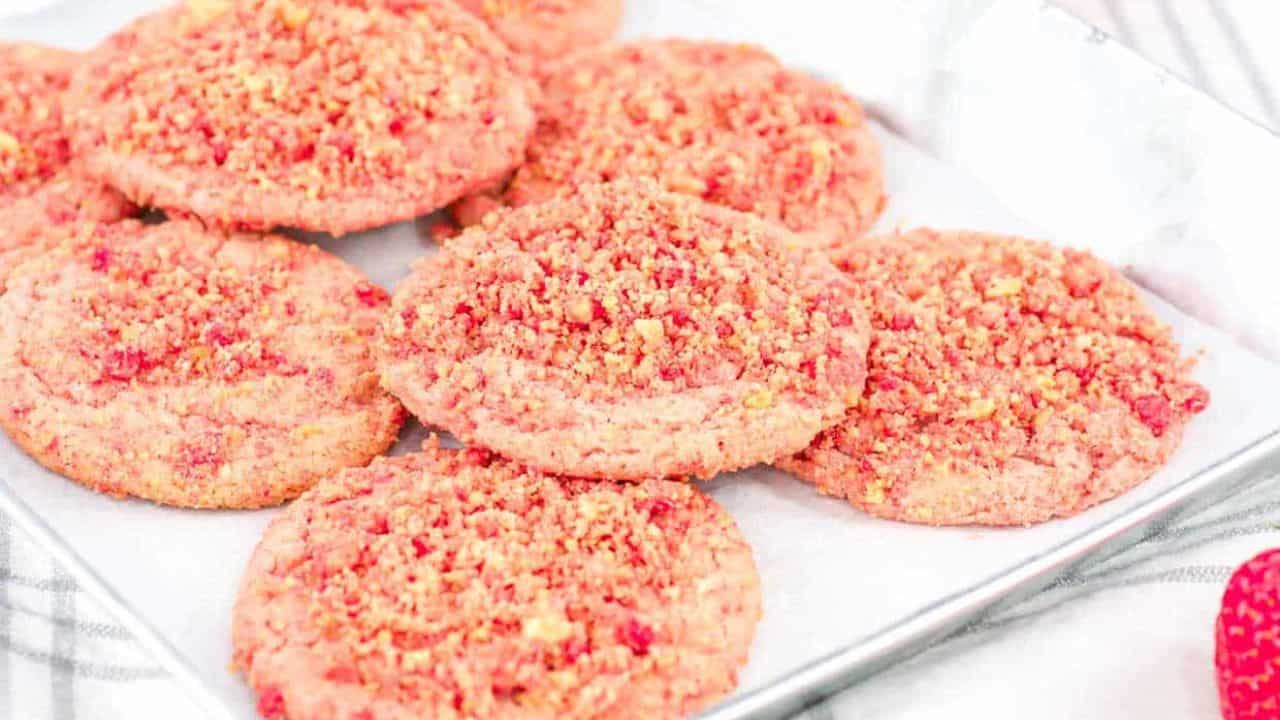 A close-up of Strawberry Crunch Cookies on a reflective metal plate, accompanied by a fresh strawberry.
