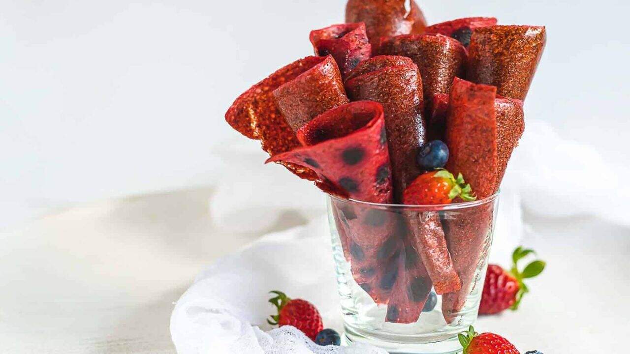 Homemade fruit roll-ups in a glass, garnished with fresh strawberries and blueberries.